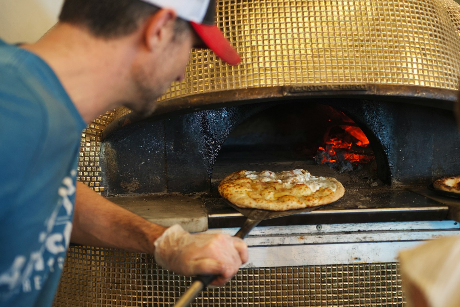 Pizzaiolo a colocar uma pizza num forno napolitano revestido a mosaico dourado