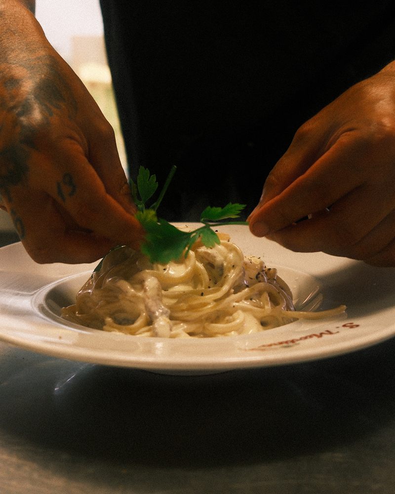 Mãos do cozinheiro a pousar salsa fresca sobre spaghetti carbonara num prato S. Martino