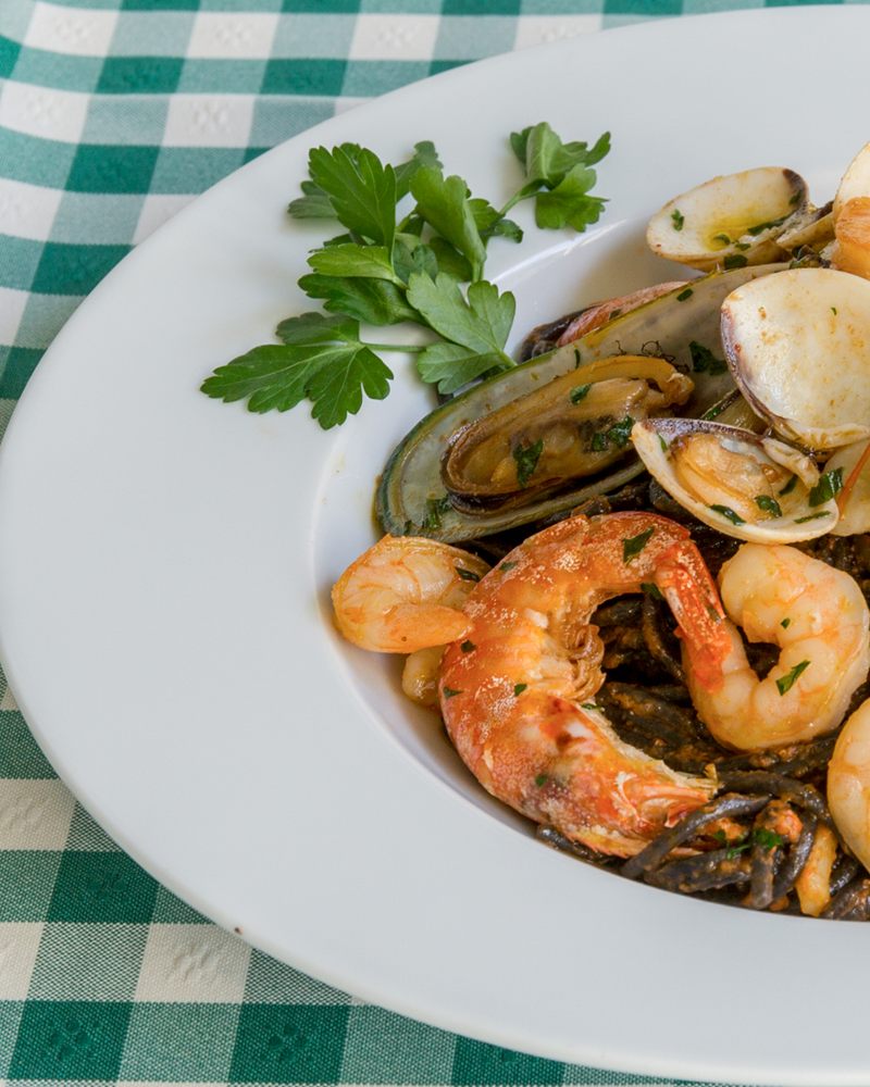 Spaghetti negro com gambas, amêijoas e mexilhões num prato branco sobre toalha aos quadrados verdes