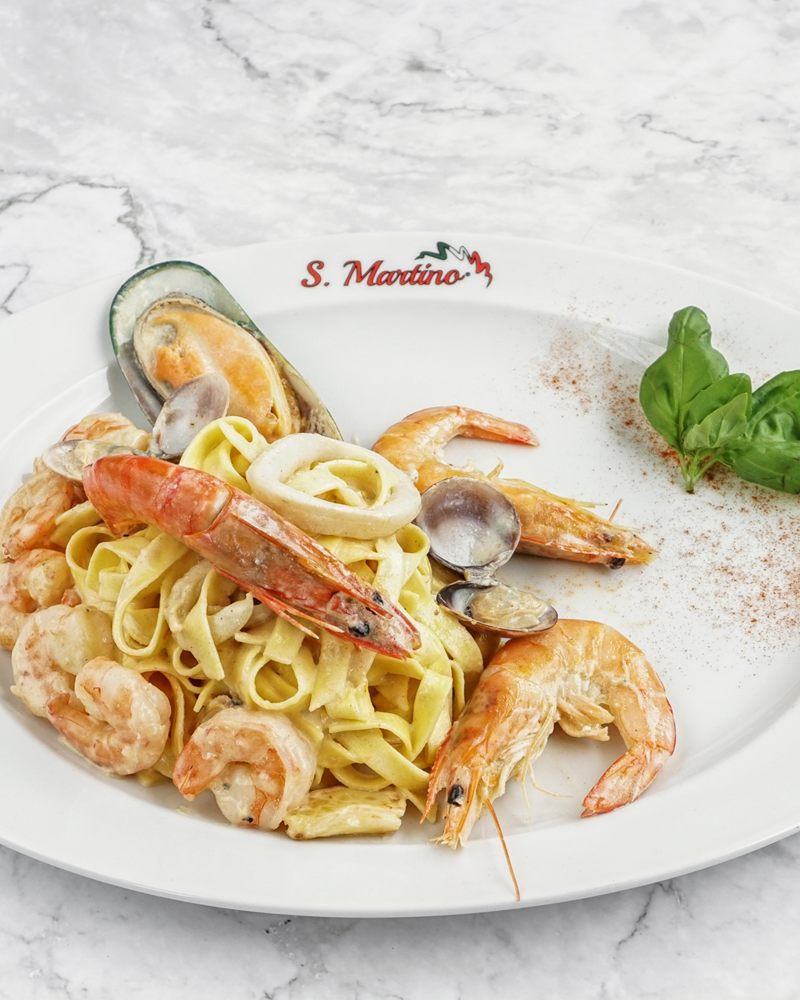 Tagliatelle com gambas, lagostins, amêijoas, mexilhão e lulas num prato S. Martino sobre mármore